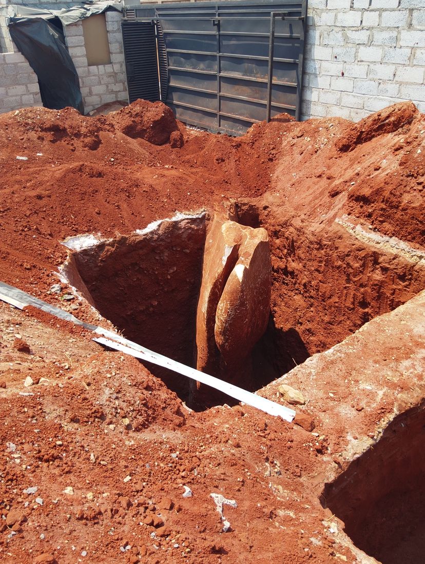 A solid reddish boulder standing in the cistern pit beside the house